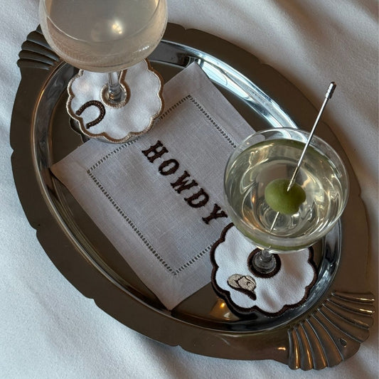Two cocktails on a silver tray with 'HOWDY' napkin and text 'ROMANTICIZE EVERYTHING'.